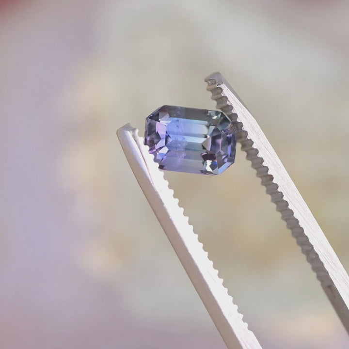 Close-up video of 1.60ct teal green purple Tanzanite emerald cut held in tweezers, precision step cut gemstone from Tanzania displaying sharp facet reflections and natural sparkle