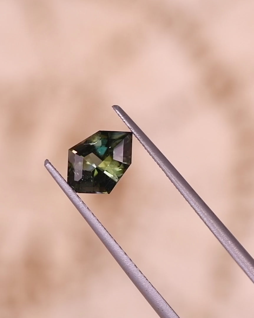 Video of 1.05CT tanzanite rotating in tweezers, revealing flashes of yellow, green, and blue light through its geometric mix cut shield design, natural unheated gemstone from Merelani Hills, Tanzania.