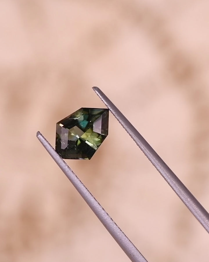 Video of 1.05CT tanzanite rotating in tweezers, revealing flashes of yellow, green, and blue light through its geometric mix cut shield design, natural unheated gemstone from Merelani Hills, Tanzania.
