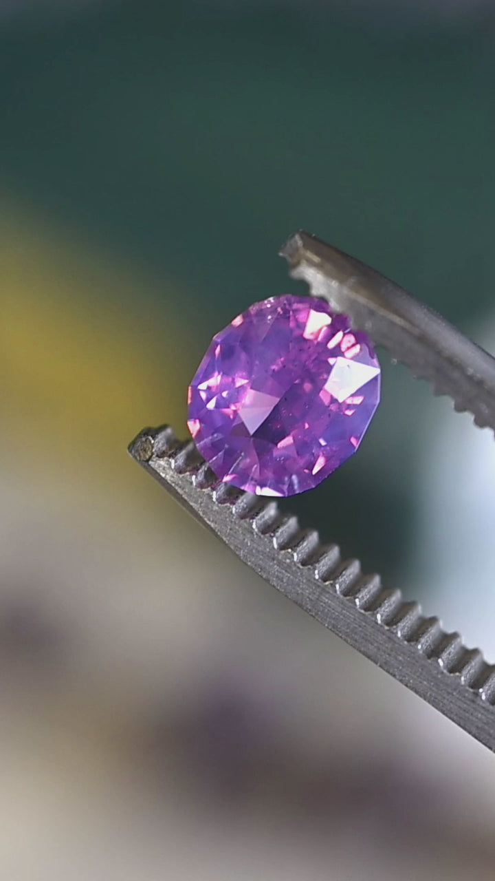 Loose opalescent purple pink sapphire turning in tweezers, revealing soft violet undertones and lively pastel reflections.