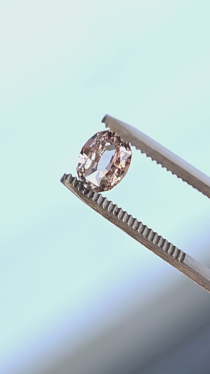 2.56ct blush peach pink antique style oval cut sapphire from Madagascar rotating in gem tweezers under natural light.