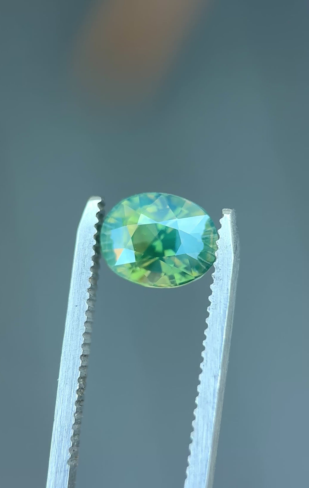 Natural Madagascar parti sapphire turning in tweezers, showcasing teal, blue, and green color zoning with exceptional brilliance.