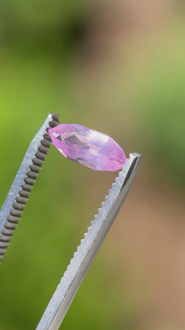 Video of 1.50CT bubblegum pink sapphire rotating in gemstone tweezers under natural sunlight, showcasing vibrant color, precision faceting, and shimmer of the marquise mixed cut, untreated sapphire from Sakaraha, Madagascar.