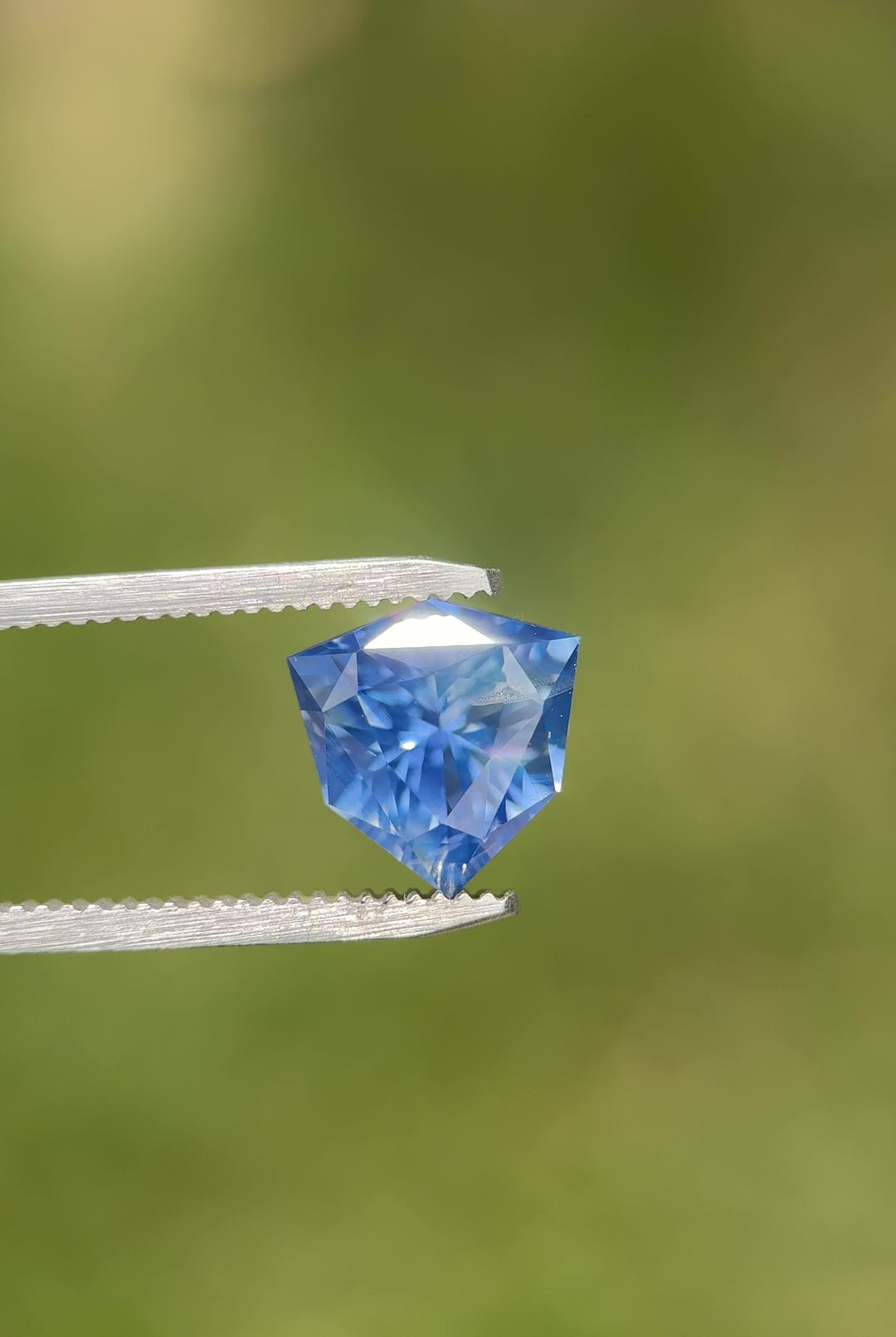 Macro video of 5.10 carat bright blue sapphire resting on fingertips, displaying vivid color flashes, faceted reflections, and the exceptional craftsmanship of the precision custom trillion shield mix cut, untreated sapphire from Madagascar.