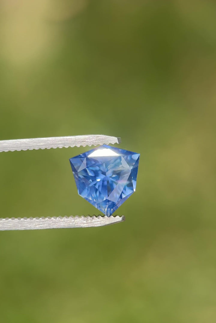 Macro video of 5.10 carat bright blue sapphire resting on fingertips, displaying vivid color flashes, faceted reflections, and the exceptional craftsmanship of the precision custom trillion shield mix cut, untreated sapphire from Madagascar.