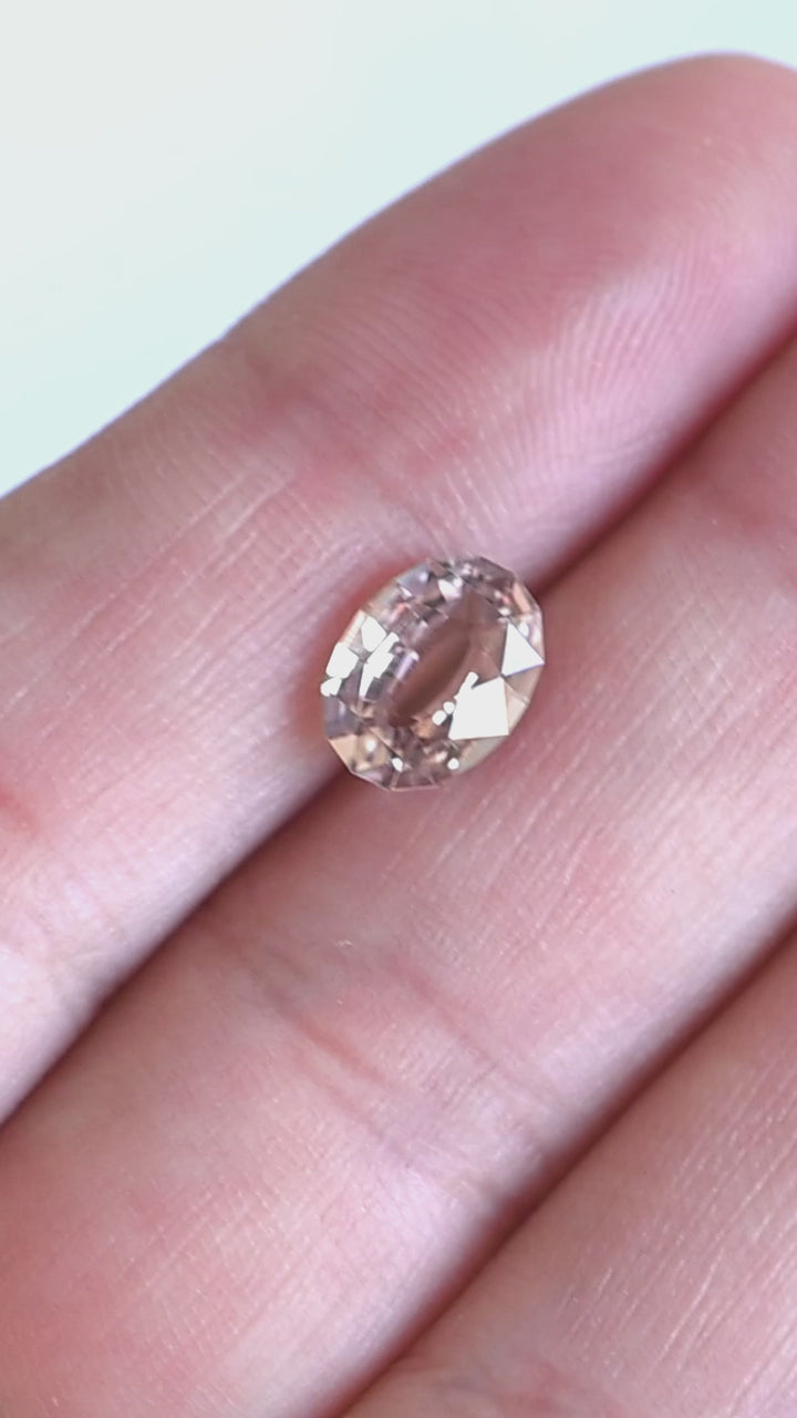 2.56ct blush peach pink antique style oval cut sapphire from Madagascar rotating on fingertips under natural light.