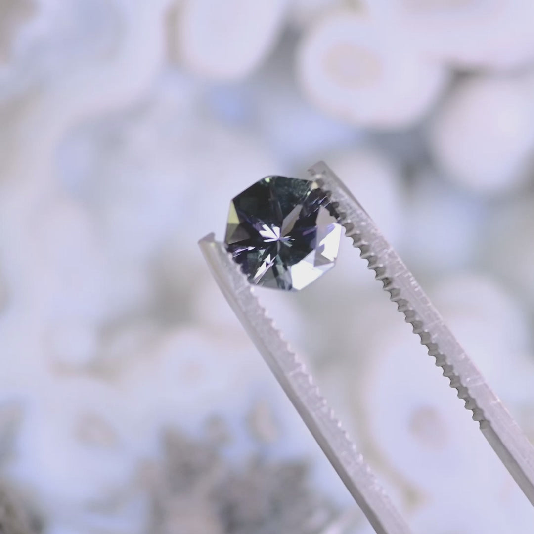 Close-up video of 1.49ct teal lavender purple Tanzanite octagon held in tweezers, precision cut gemstone from Tanzania displaying brilliance, clarity and geometric facet pattern