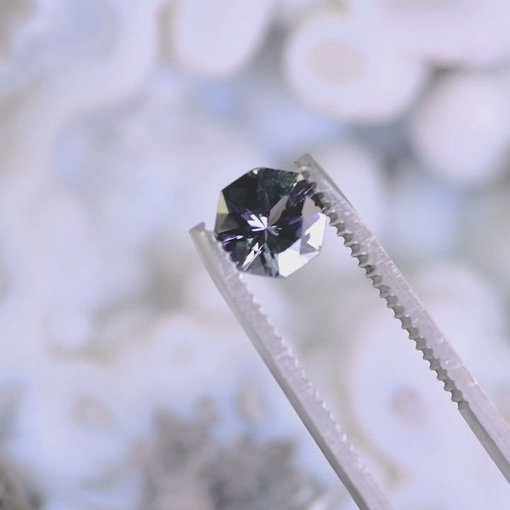 Close-up video of 1.49ct teal lavender purple Tanzanite octagon held in tweezers, precision cut gemstone from Tanzania displaying brilliance, clarity and geometric facet pattern