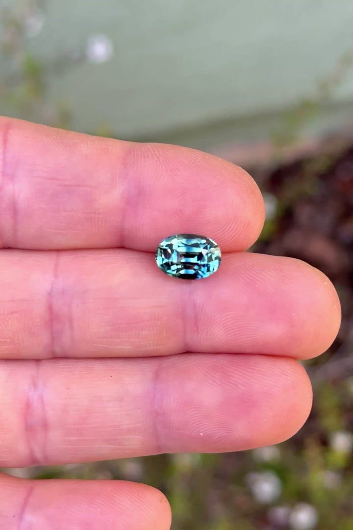 4.24ct parti green teal blue sapphire rotating in hand, revealing dramatic color zoning and bright precision-cut reflections.