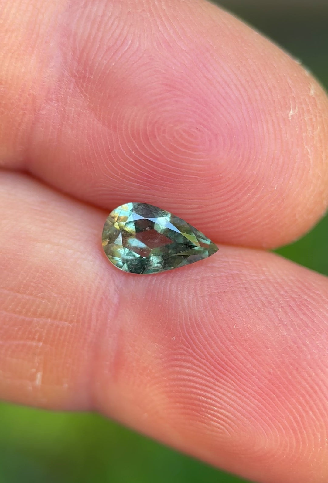 Handheld video of untreated sage teal green 1.06ct sapphire in pear shape, revealing its color play and clarity in natural light