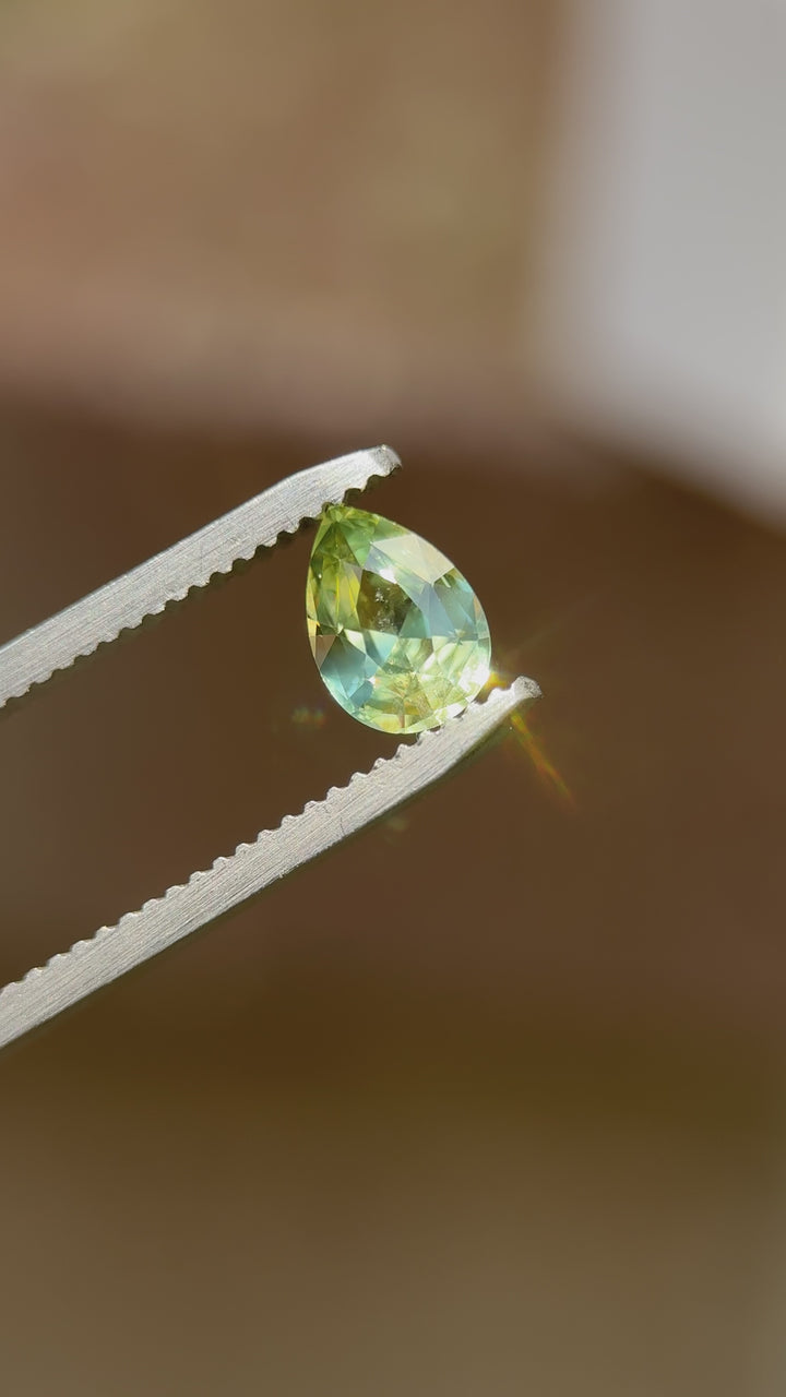 Rotating view of a 1.07ct pear brilliant sapphire displaying shifting colors of teal, yellow, and blue under natural light.