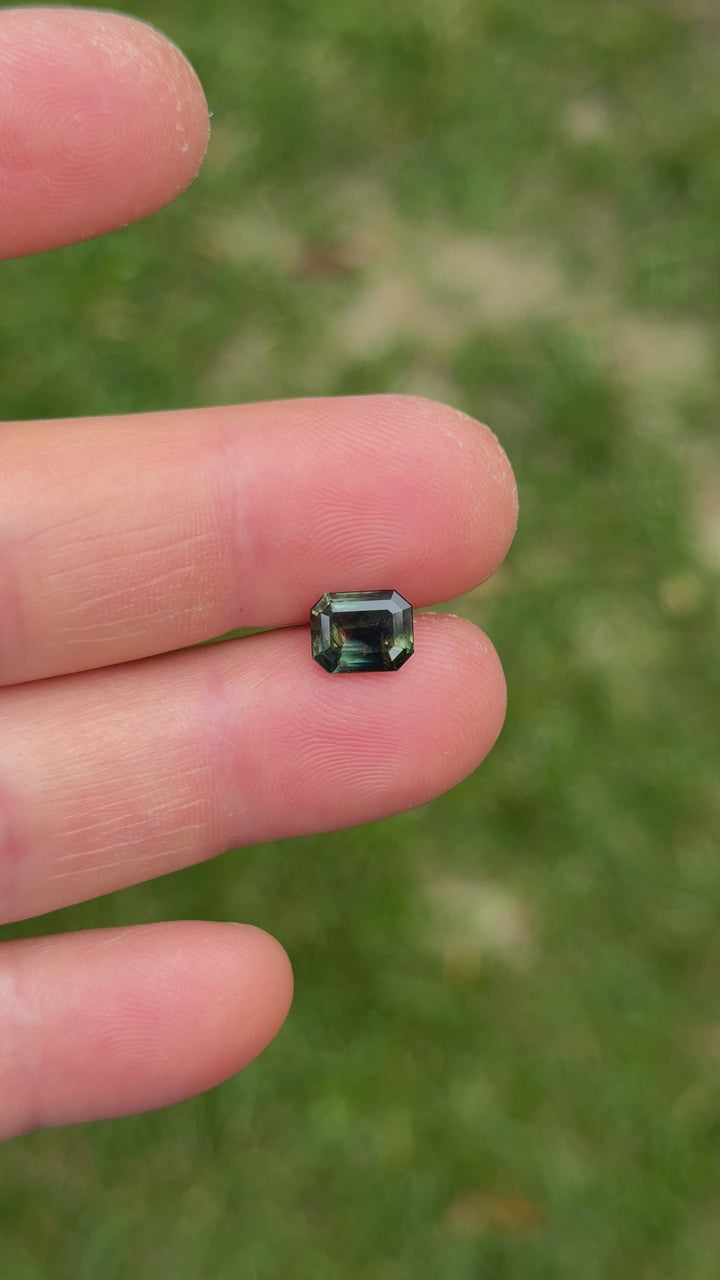Macro video of modified emerald cut sapphire under natural light, showing complex color zoning and clarity.