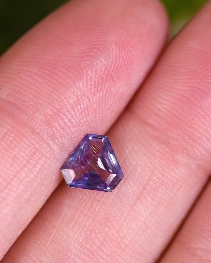 Close-up motion video of 1.05 carat violet aqua blue sapphire turning under natural light, showcasing reflective geometry and sparkle of its custom cut corner trillion mix cut, untreated gem from Umba River, Tanzania.