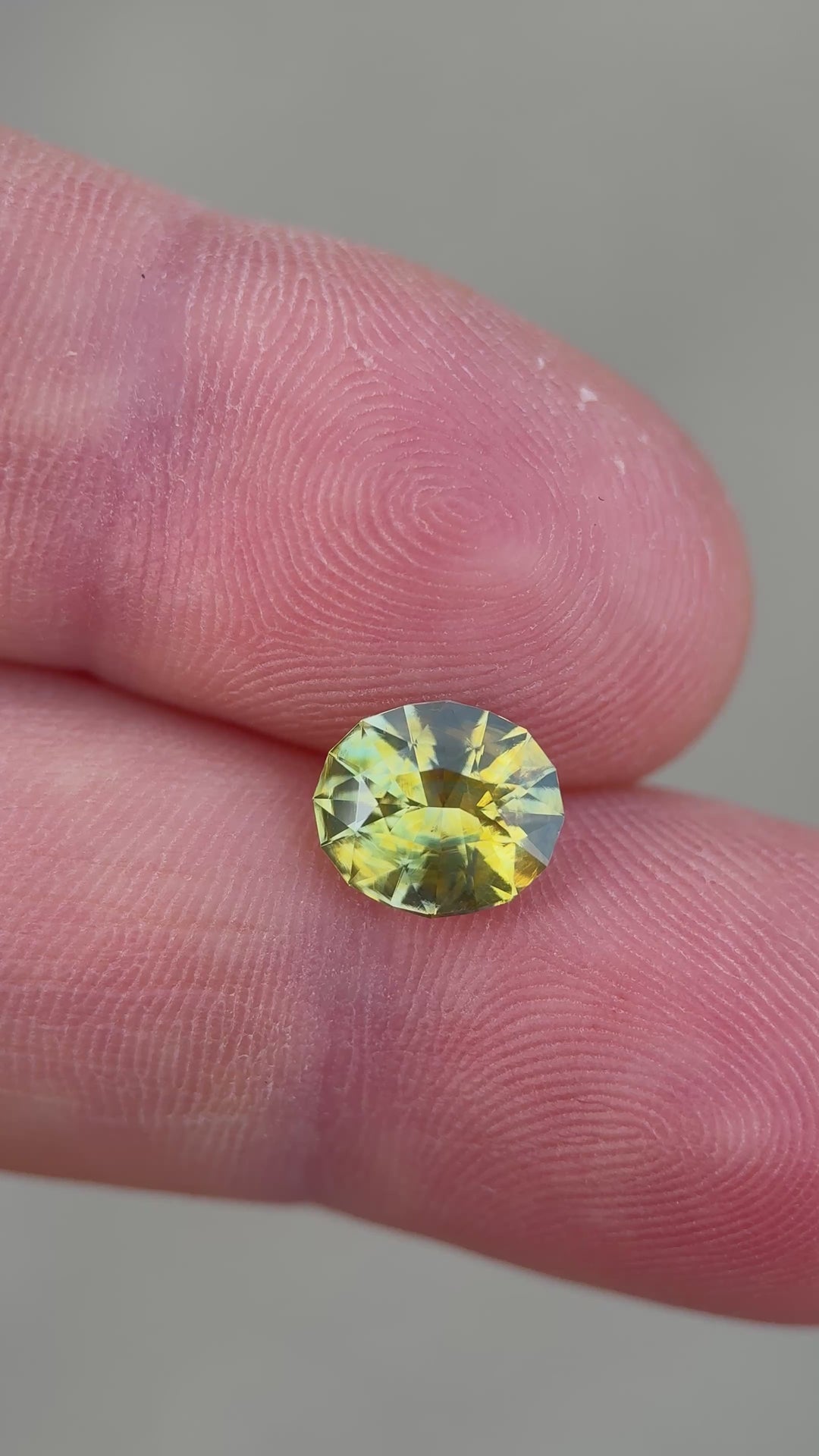 2.52ct parti yellowish green sapphire rotating in hand, revealing shifting olive, green, and golden flashes across the modified oval cut.