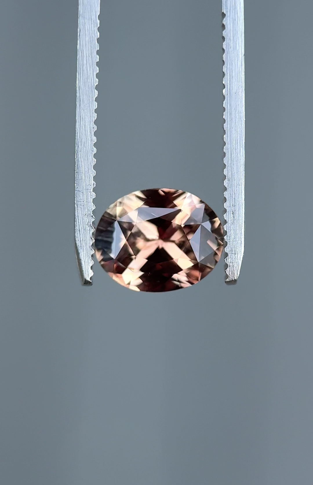 rotating 3.04 carat pumpkin spice autumn color shift sapphire oval precision mixed cut from Madagascar showing purplish reddish brown tones in tweezers