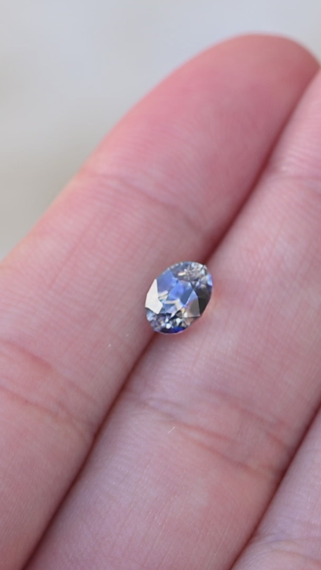 1.60ct blue and white bi color parti sapphire from Sri Lanka rotating on finger tips under natural light.