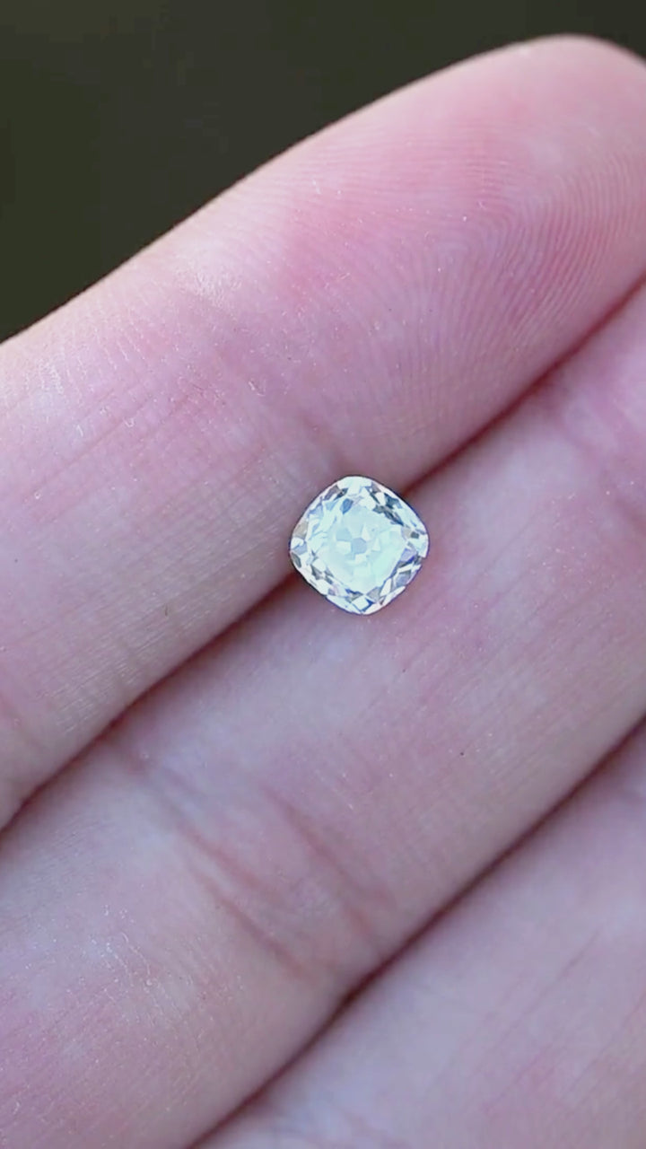 A 0.92 carat white antique-style cushion cut diamond rotating on fingertips in natural light, revealing broad flashes, soft vintage brilliance, and balanced proportions.
