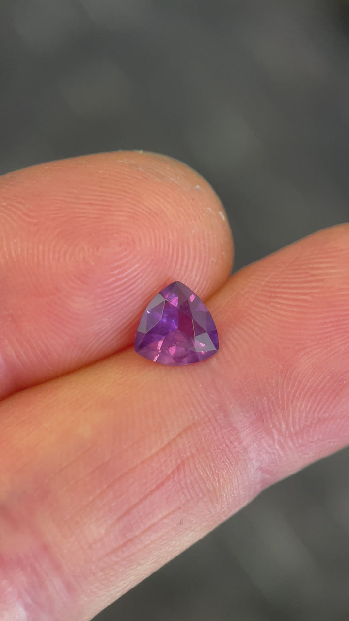 Video showing the brilliance and color shift of a 0.94-carat trillion cut pink-purple sapphire from Tanzania, captured in natural lighting.