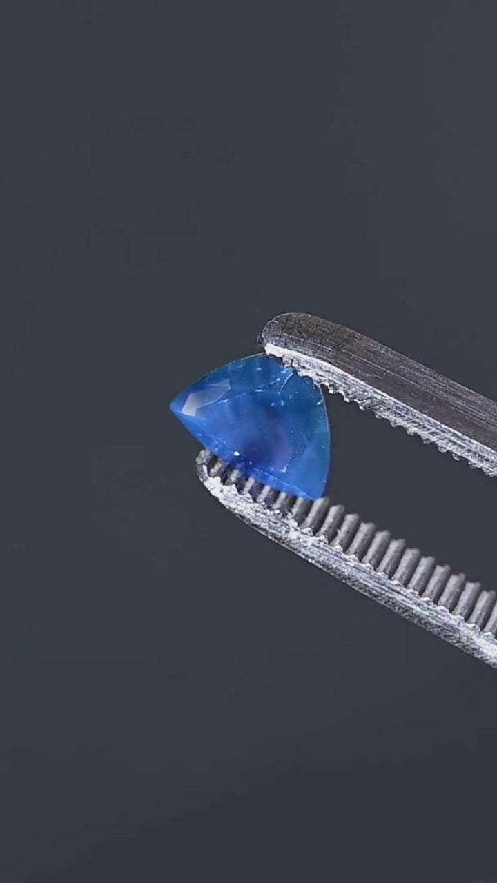 Explore the custom trillion cut of this untreated 1.91ct opalescent royal blue sapphire from Nigeria. Presented in jeweler's tweezers, the gemstone features a rich blue body color, fine internal linear features and a distinctive triangular silhouette.