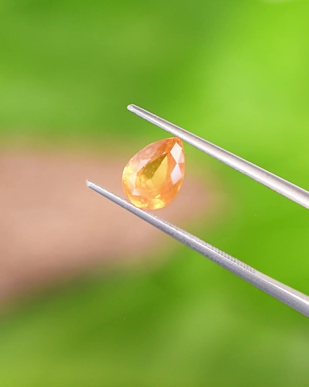 Video of 1.59CT orange red-orange yellow sapphire rotating in gemstone tweezers, showing shifting fiery hues and the intricate brilliance of the modified pear cut, unheated sapphire from Umba River, Tanzania.