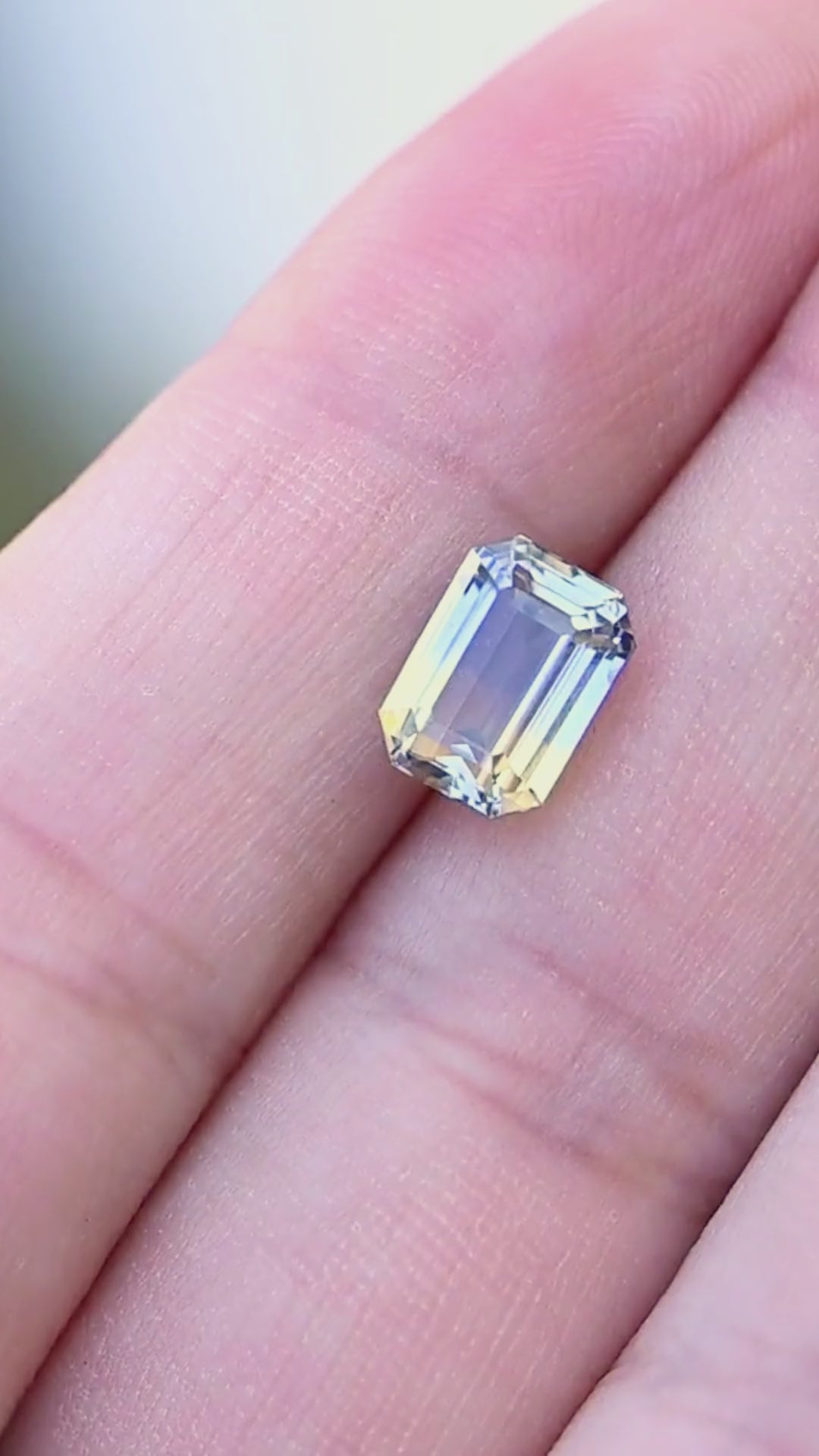 3.03 carat Sri Lankan parti sapphire moving on a hand, revealing shifting bands of blue, pale yellow and silvery reflections through its precision emerald-cut facets.