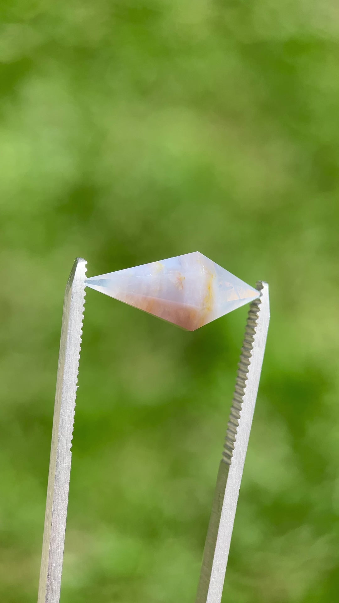 Slow rotating video of faceted 8.00 carat periwinkle sapphire against greenery, emphasizing clarity, cut, and natural zoning.