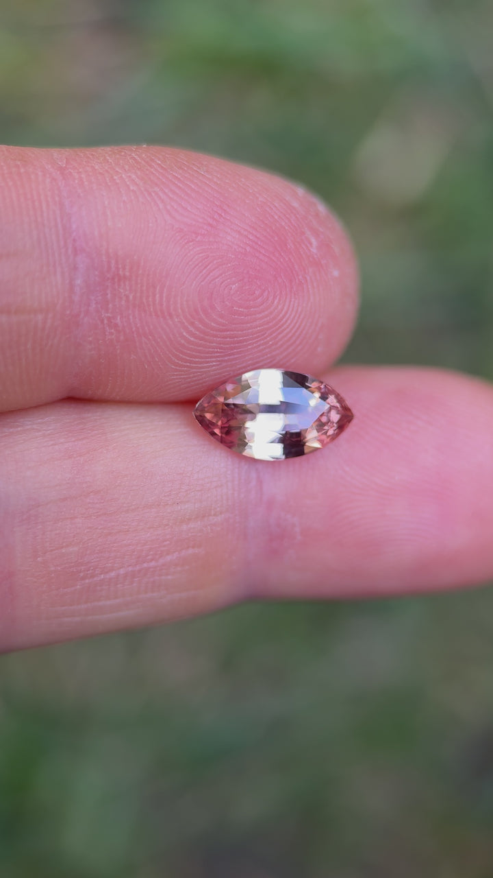 Close-up video of a 2.57ct marquise-cut peach pink champagne sapphire being tilted in hand to reveal brilliance, facet reflections, and warm parti hues; ethically sourced from Sakaraha, Madagascar.