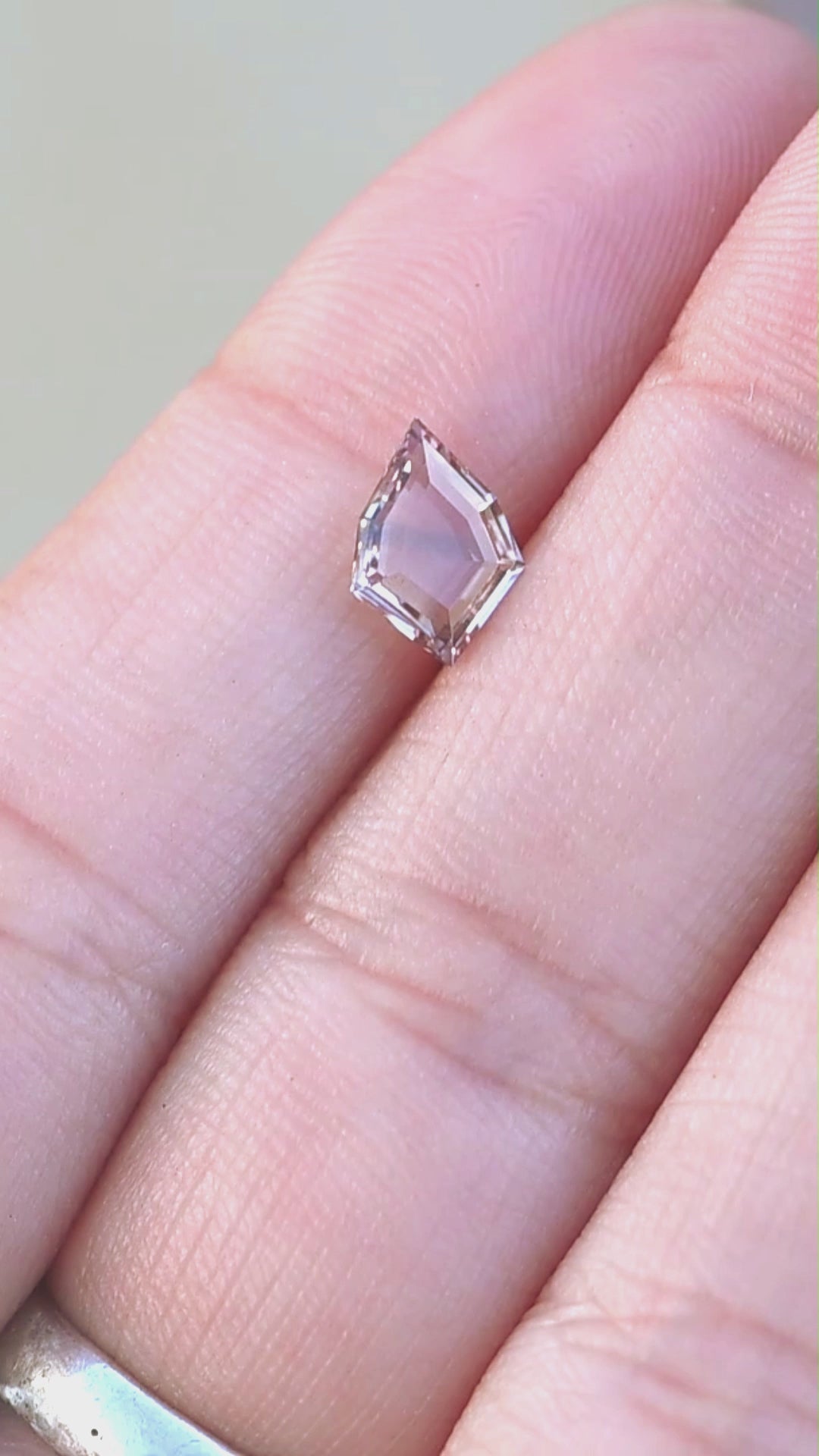 1.12ct peach and blue parti portrait cut sapphire rotating on finger tips under natural open shade lighting.