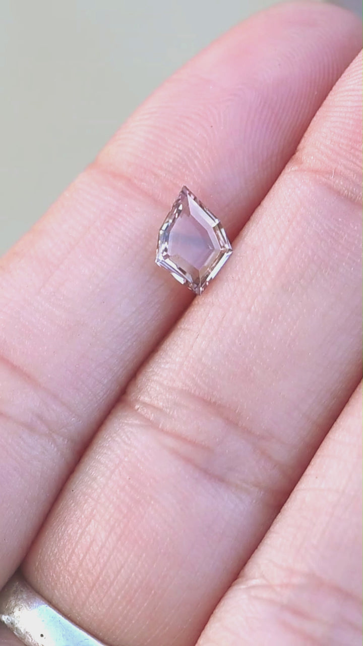 1.12ct peach and blue parti portrait cut sapphire rotating on finger tips under natural open shade lighting.