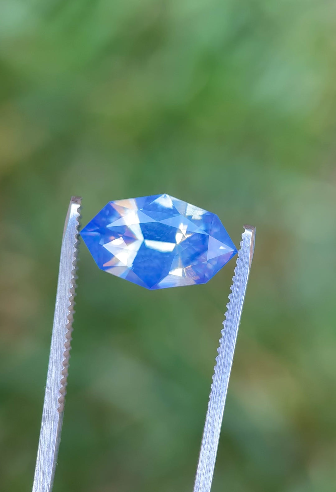 Video of 6.07CT opalescent periwinkle blue sapphire rotating in gemstone tweezers, showing flashes of light and color transitions through the precision custom marquise mixed cut, unheated sapphire from Sakaraha, Madagascar.
