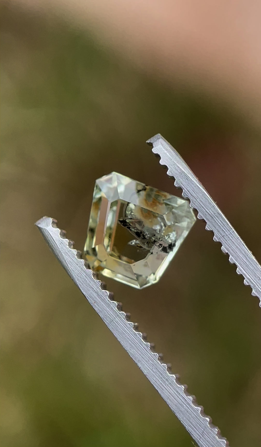 A 1.68-carat earthy yellow-green sapphire in a custom shield tablet cut, rotated in tweezers to showcase its brilliance, clarity, and intricate shape.