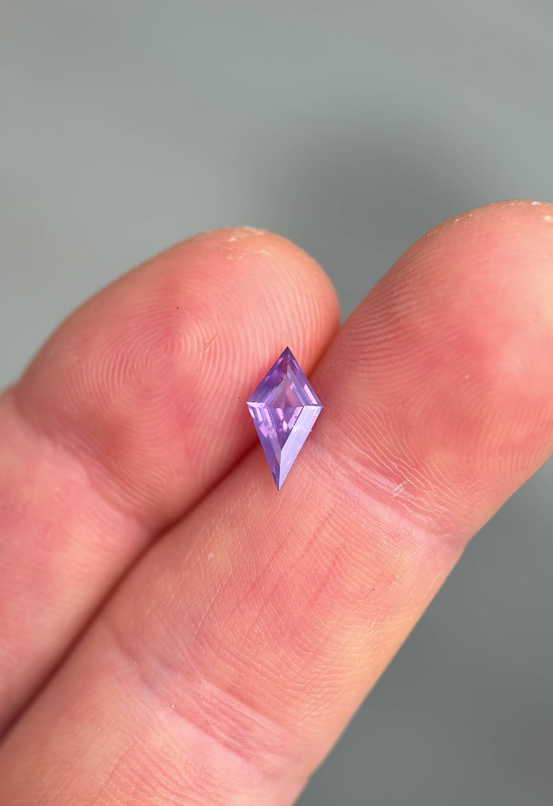 Loose opalescent sapphire with precision kite cut faceting resting on fingertips showing off natural color zoning and opalescence under natural light.