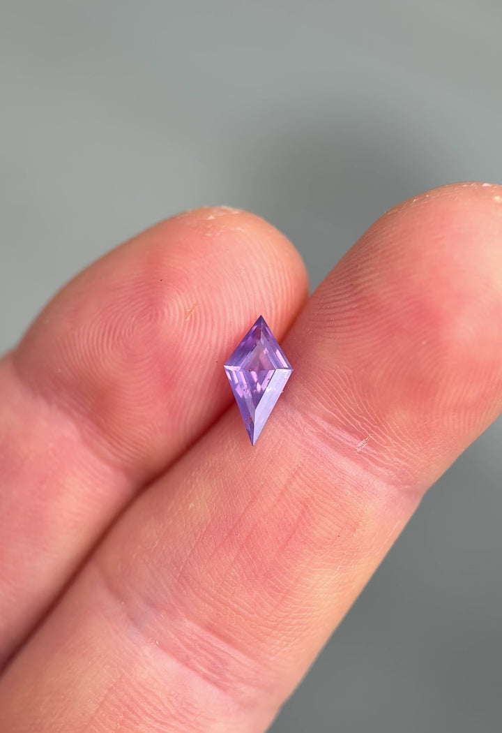 Loose opalescent sapphire with precision kite cut faceting resting on fingertips showing off natural color zoning and opalescence under natural light.