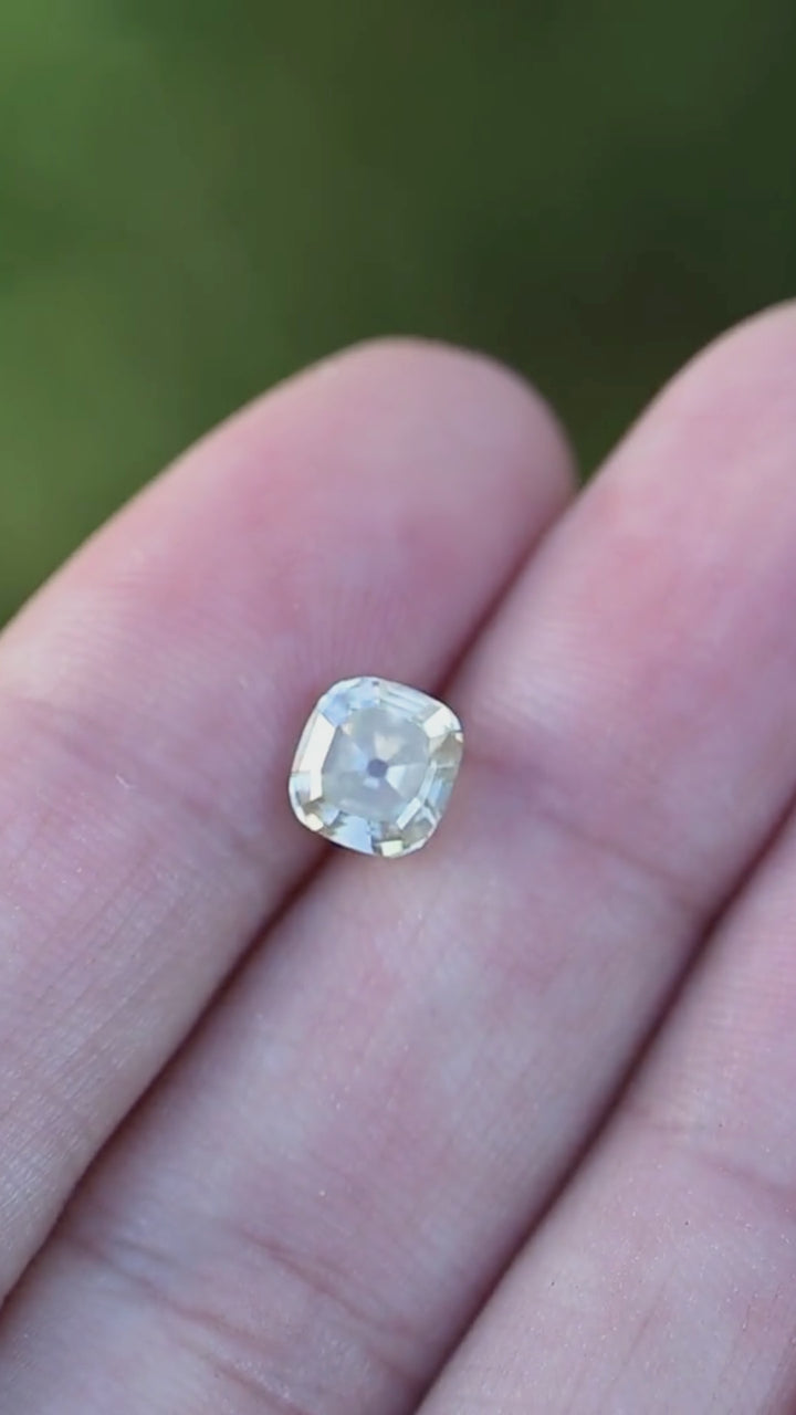 A 1.60 carat yellow antique-style cushion cut diamond rotating in natural light on fingertips, revealing warm honey tones, broad flashes, and vintage-inspired faceting.
