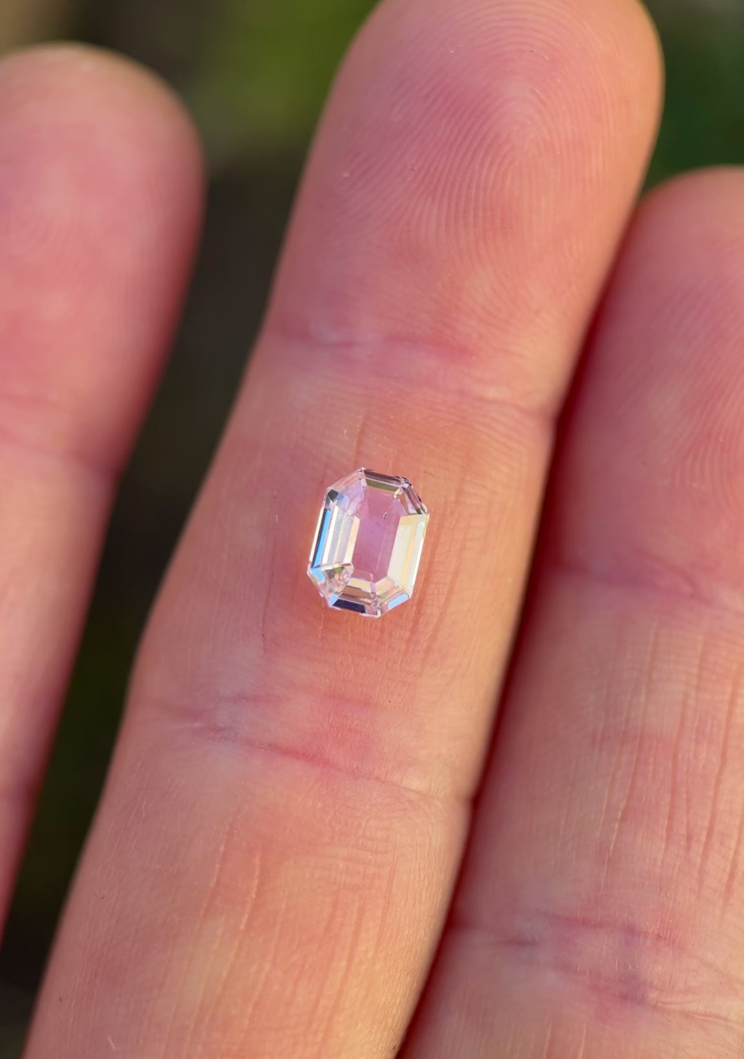 Close-up video of 1.50 carat blush pink sapphire resting on fingertips, showcasing light movement across the antique emerald cut facets and the natural beauty of this untreated sapphire from Madagascar.