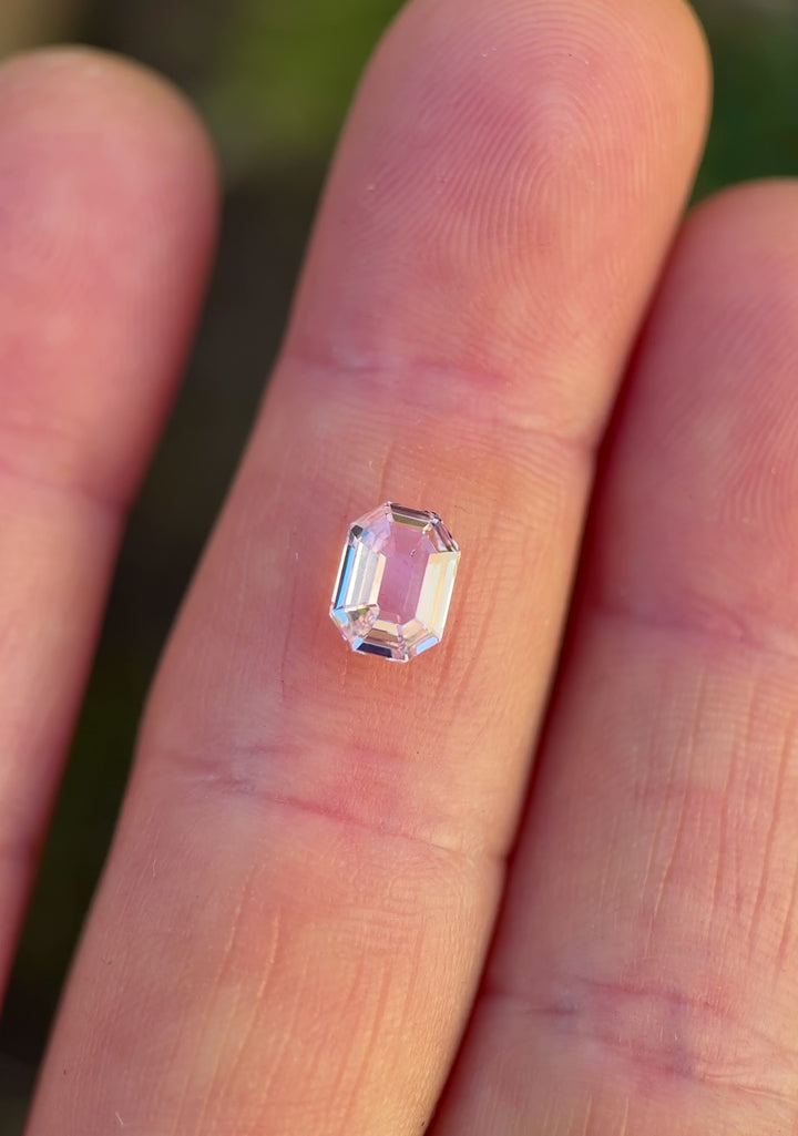 Close-up video of 1.50 carat blush pink sapphire resting on fingertips, showcasing light movement across the antique emerald cut facets and the natural beauty of this untreated sapphire from Madagascar.