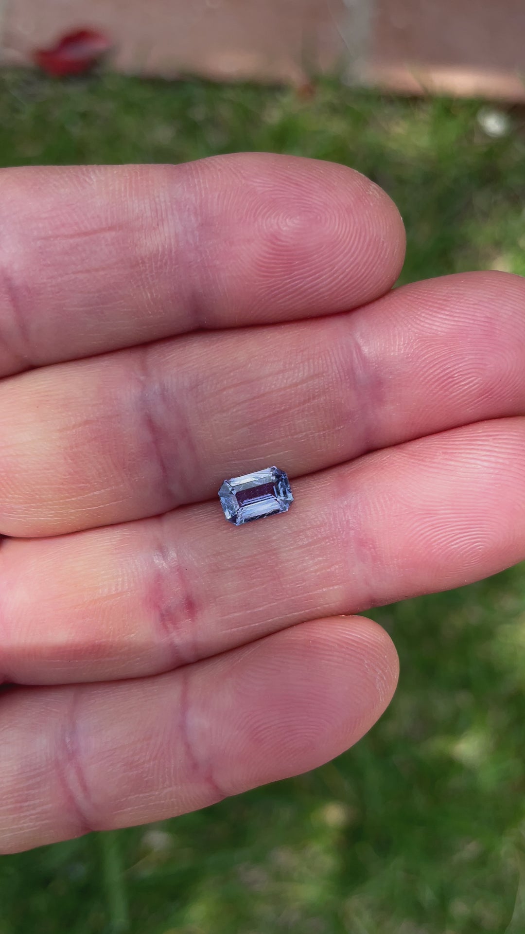 A video of a 1.26-carat sapphire, violet-blue in color, shown in hand to highlight its dimensions (7.50 x 4.97 x 3.21 mm) and modified emerald cut under natural lighting.