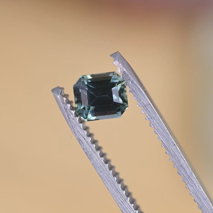 Loose emerald cut sapphire turning in tweezers, revealing natural blue and green color shifts from Sakaraha, Madagascar.