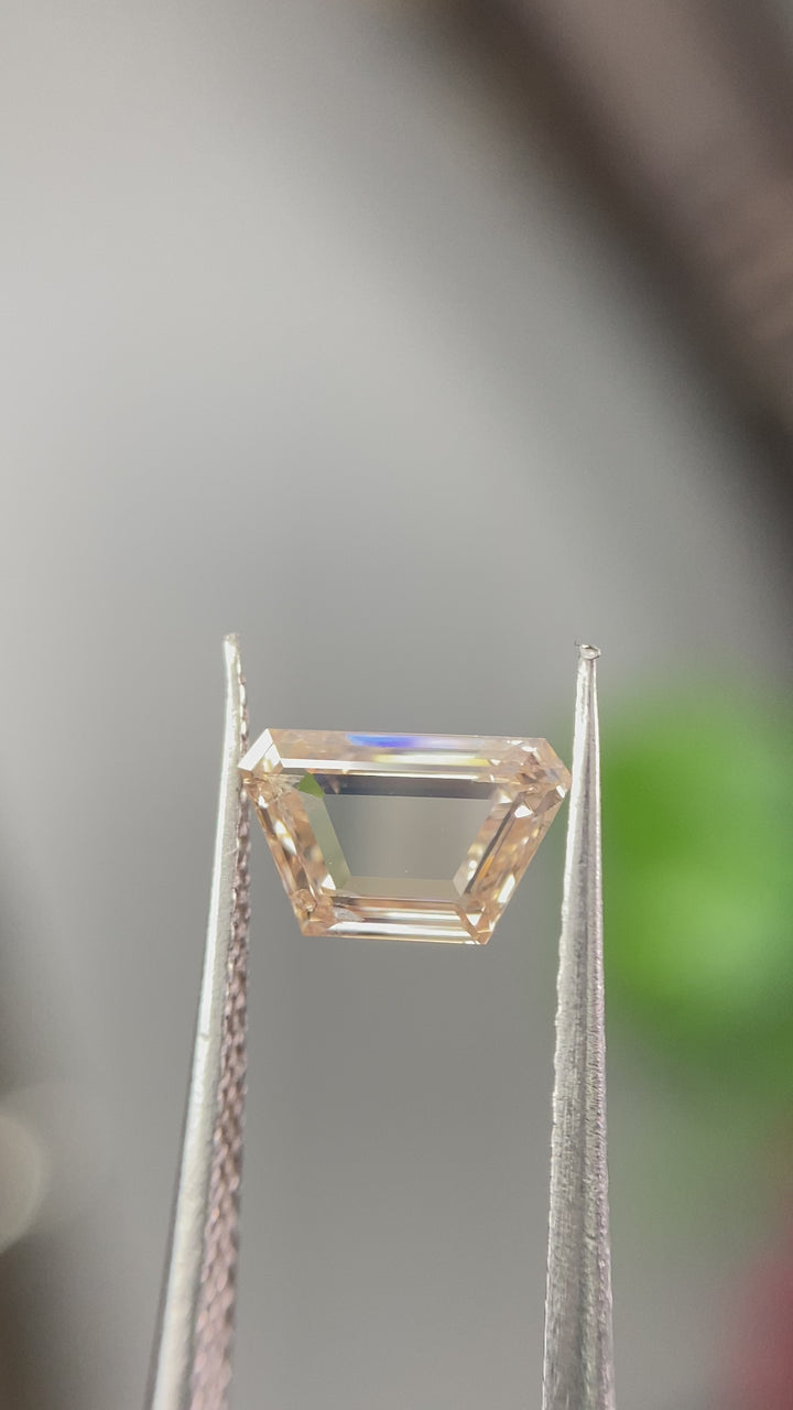 Loose natural orange pink trapezoidal portrait cut diamond rotating in gem tweezers under natural light