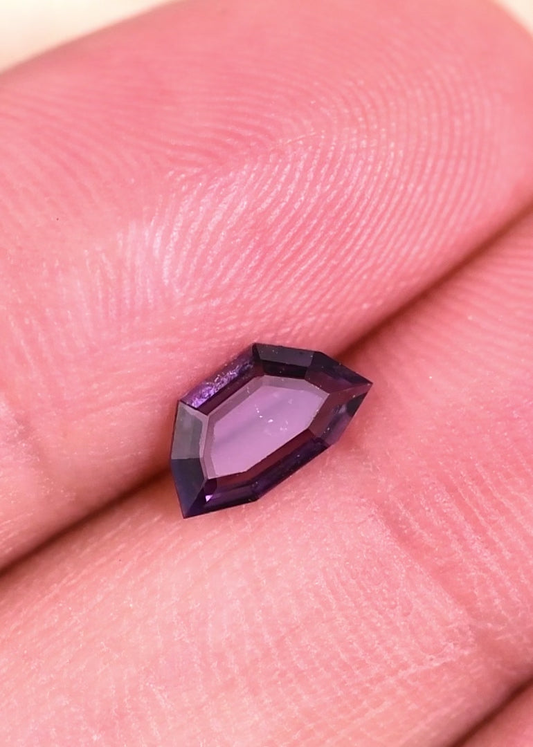 Close-up video of 0.70 carat Sri Lanka spinel on hand, purple and pink tones intensifying under light in a geometric portrait step cut design