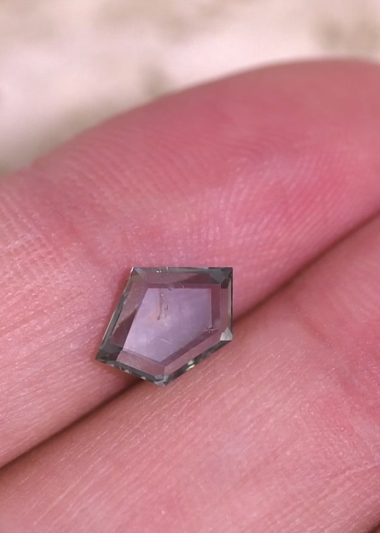 Close-up video of an untreated Montana sapphire held in tweezers, demonstrating color shift from teal blue seafoam to purple and the symmetry of the geometric pentagon portrait cut.