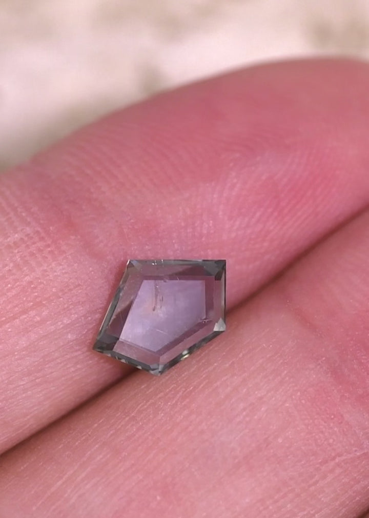 Close-up video of an untreated Montana sapphire held in tweezers, demonstrating color shift from teal blue seafoam to purple and the symmetry of the geometric pentagon portrait cut.