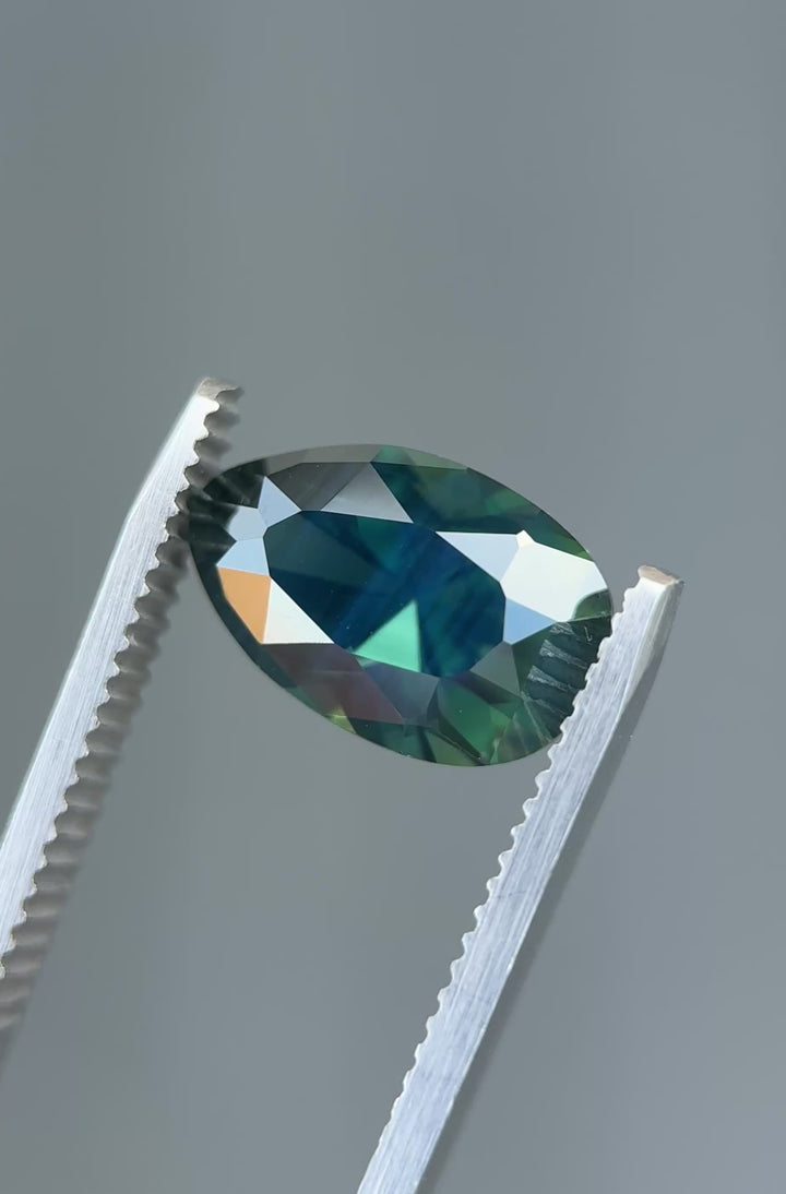 Deep teal sapphire rotating in light showing strong blue and green color zoning and brilliance.