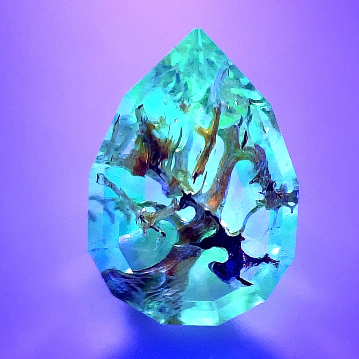 A stunning 4.18-carat Hyalite Opal from Mexico, showcasing its step cut pear shape. The opal's clear and white hues shimmer under natural light, while its fluorescence creates a mesmerizing glow in UV light.