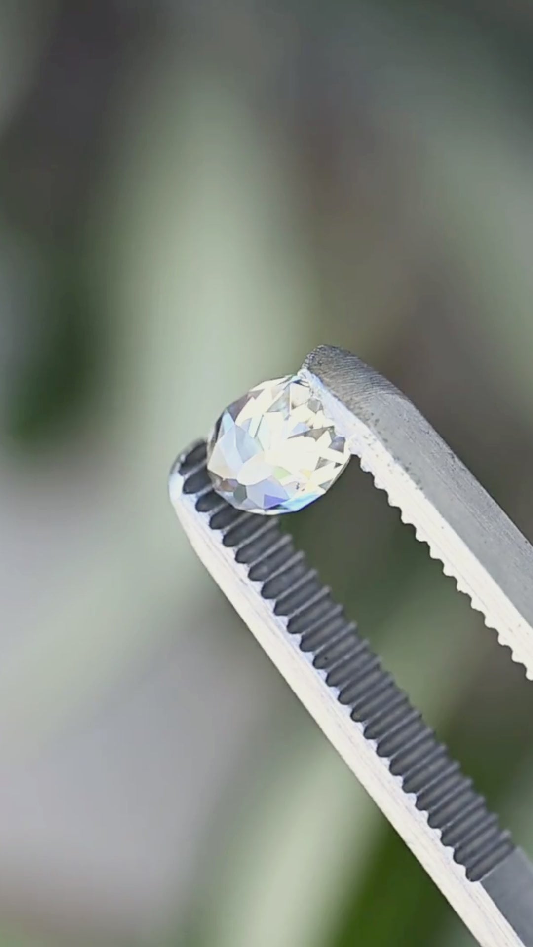 1.09 carat untreated oval Mughal cut diamond rotated between jeweler’s tweezers, showing the elongated outline, broad facets, open central table and natural inclusions from changing angles.