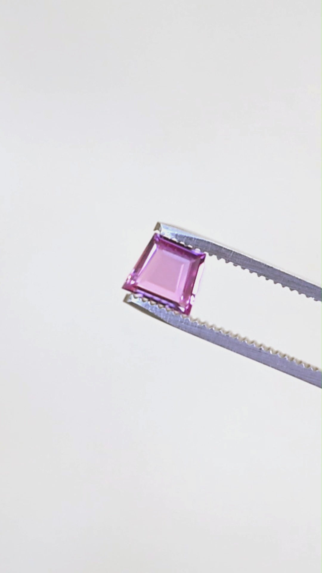 Natural hot pink portrait cut sapphire rotating in gem tweezers under natural light.