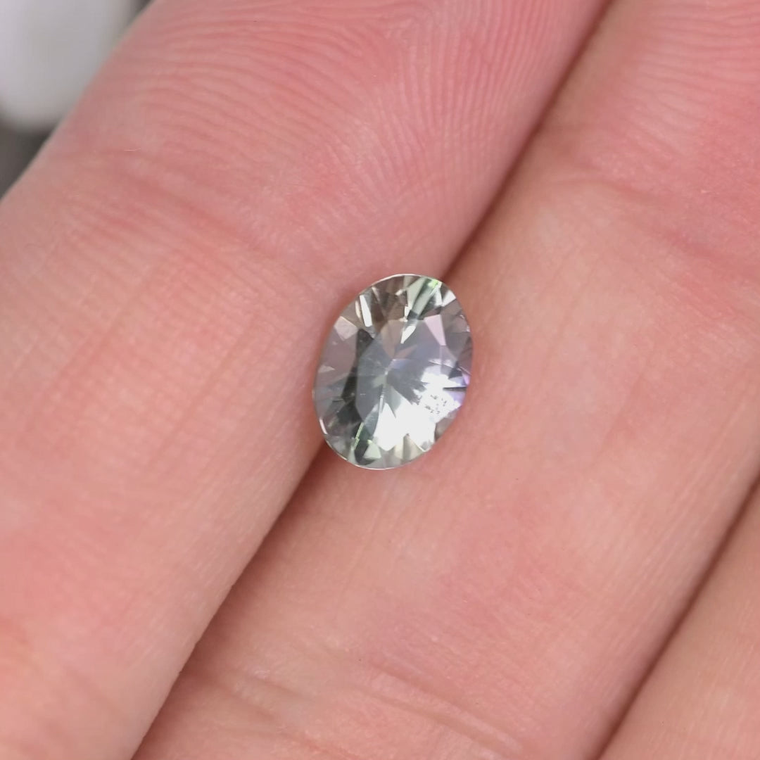 1.11 carat violet teal green oval Tanzanite rotating on hand in natural light, mix modified brilliant cut from Merelani Hills showing vivid color shift and sparkling custom jewelry brilliance