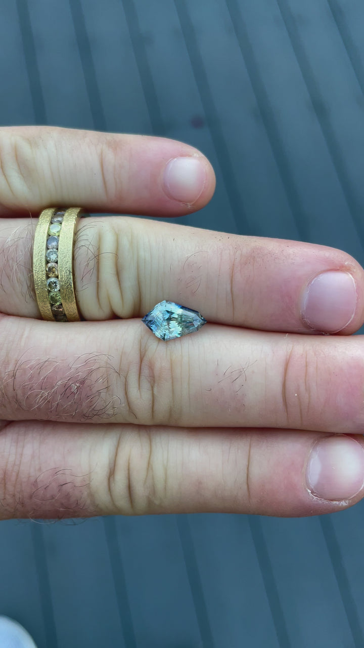A rotating video of a 2.32-carat sapphire in a geometric step-cut kite shape. The stone displays a beautiful mix of yellow and Ceylon denim blue hues, with no heat treatment, and originates from Sri Lanka. The video highlights its sharp facets and exceptional light reflection.