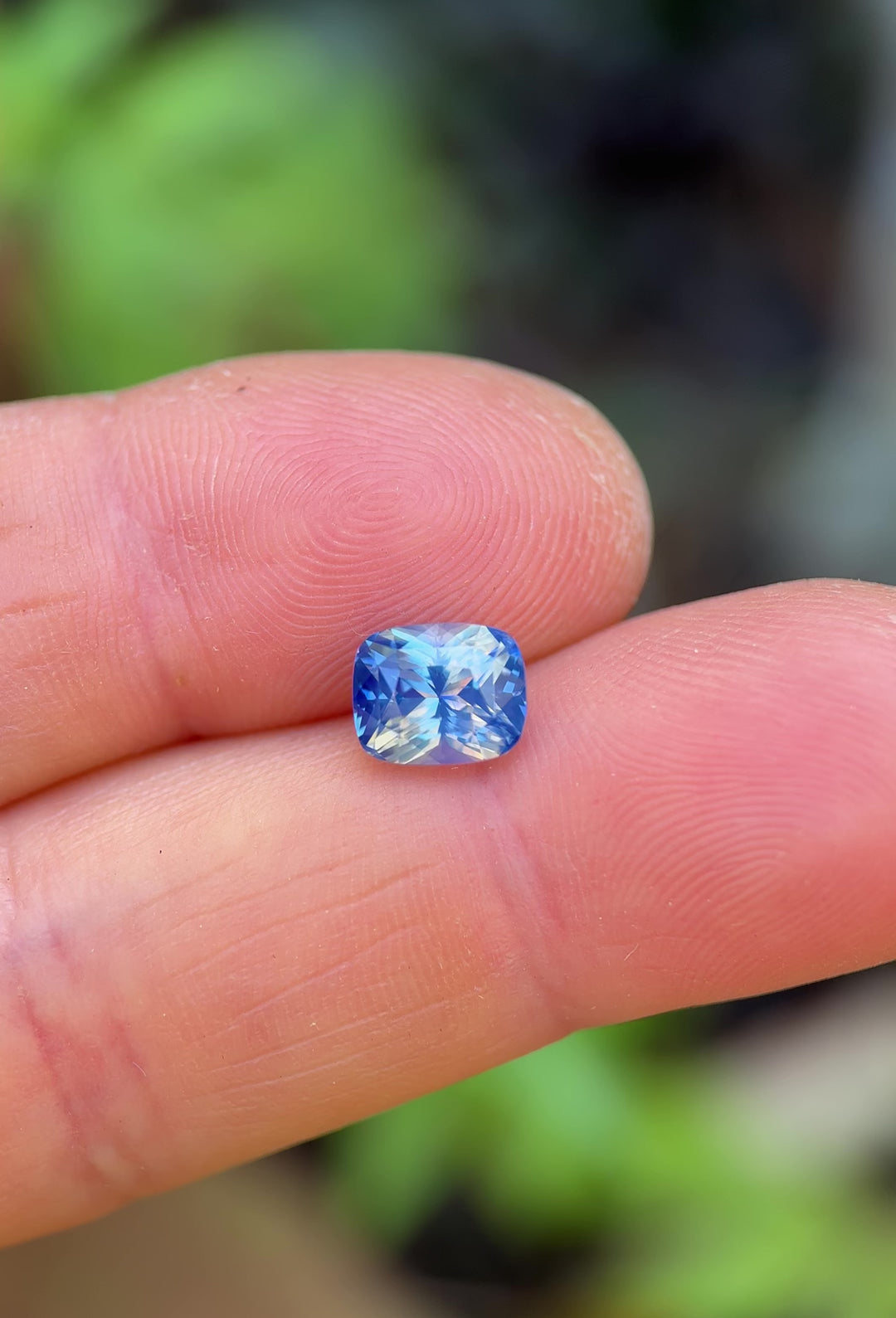 Macro video of 2.64 carat opalescent parti sapphire resting on fingertips, capturing flashes of blue and white under sunlight, revealing brilliance and clarity of the mix cushion cut, untreated sapphire from Sakaraha, Madagascar.