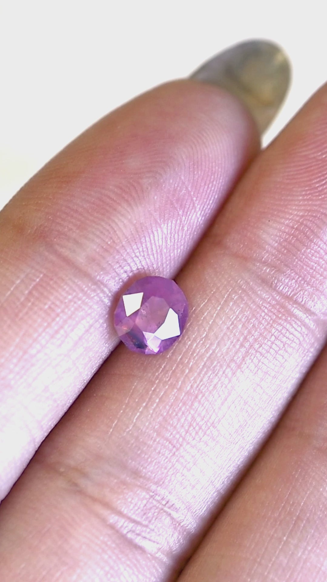 1.28ct opalescent vivid pink sapphire rotating in hand, revealing bright pink flashes and a small contrasting blue parti color zone.